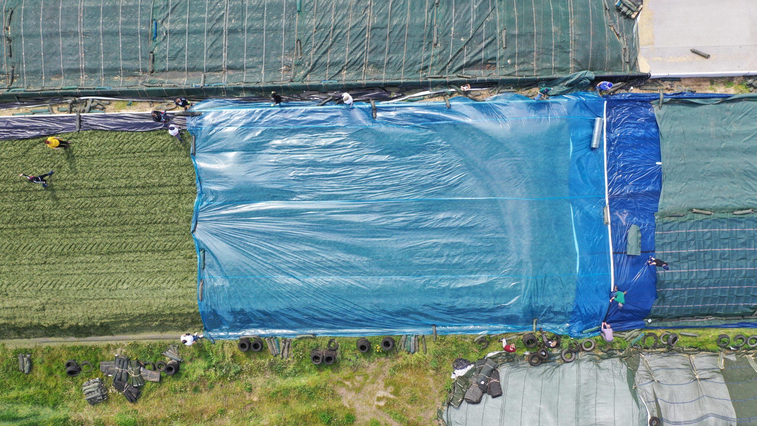 Mehrere Personen verteilen die blaue OXY Max 50 Barrierefolie auf einem Grassilo, um die Silage abzudecken und zu schützen