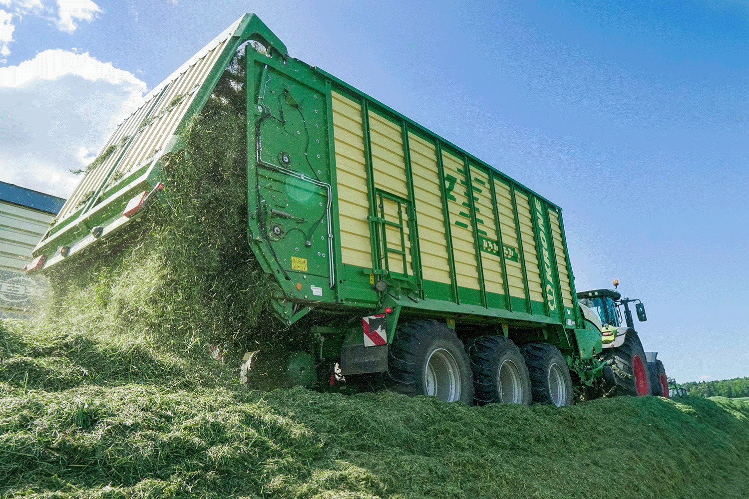 Ein Ladewagen fährt über ein Grassilo und kippt frisches Gras darauf, um es für die Silage aufzuschichten