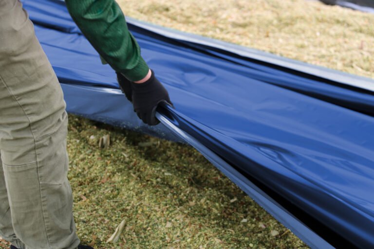 Ein Mann breitet eine blaue OXY Twin Barrierefolie auf einem Maissilo aus, um die Silage abzudecken und zu schützen