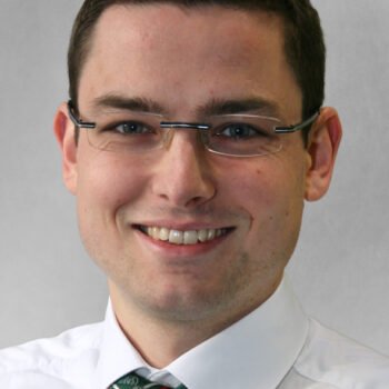 Nahaufnahme eines Mannes mit kurzen braunen Haaren und Brille, der lächelt oder lacht