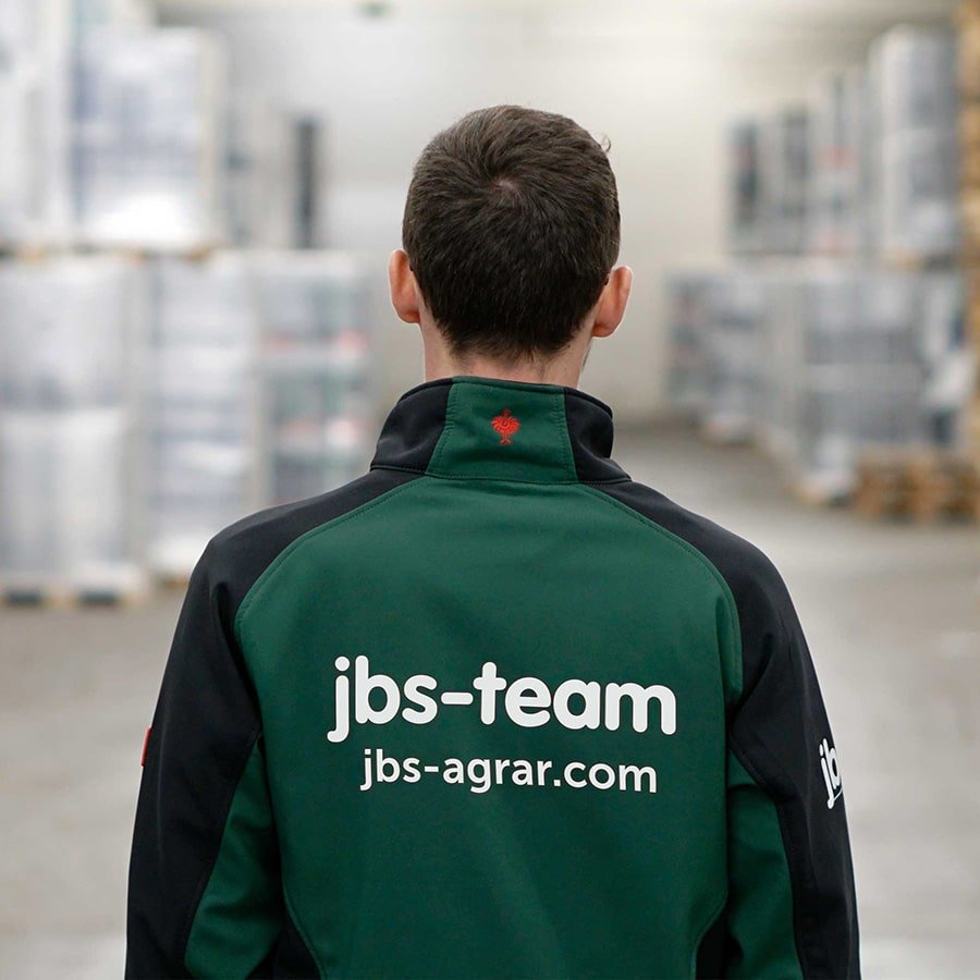 Braunhaariger Mann, er trägt eine jbs-team Jacke teils in grün und teils schwarz